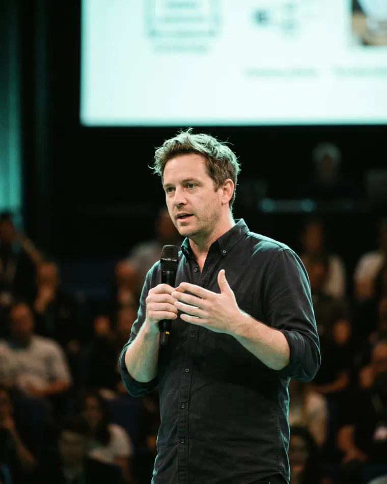 A founder speaking on a conference stage with a handheld microphone