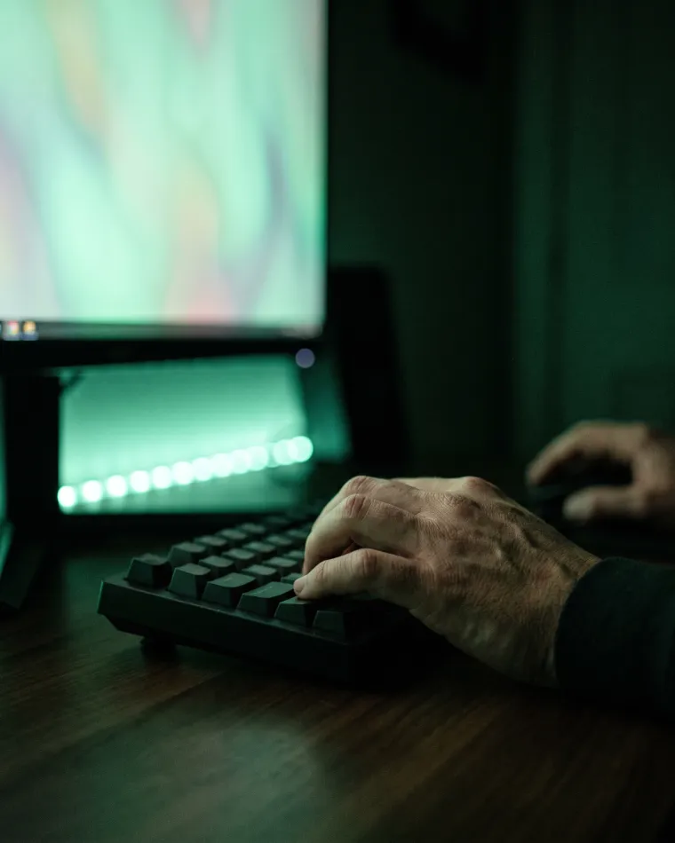 Hands on a mechanical keyboard in a dark room lit by a monitor
