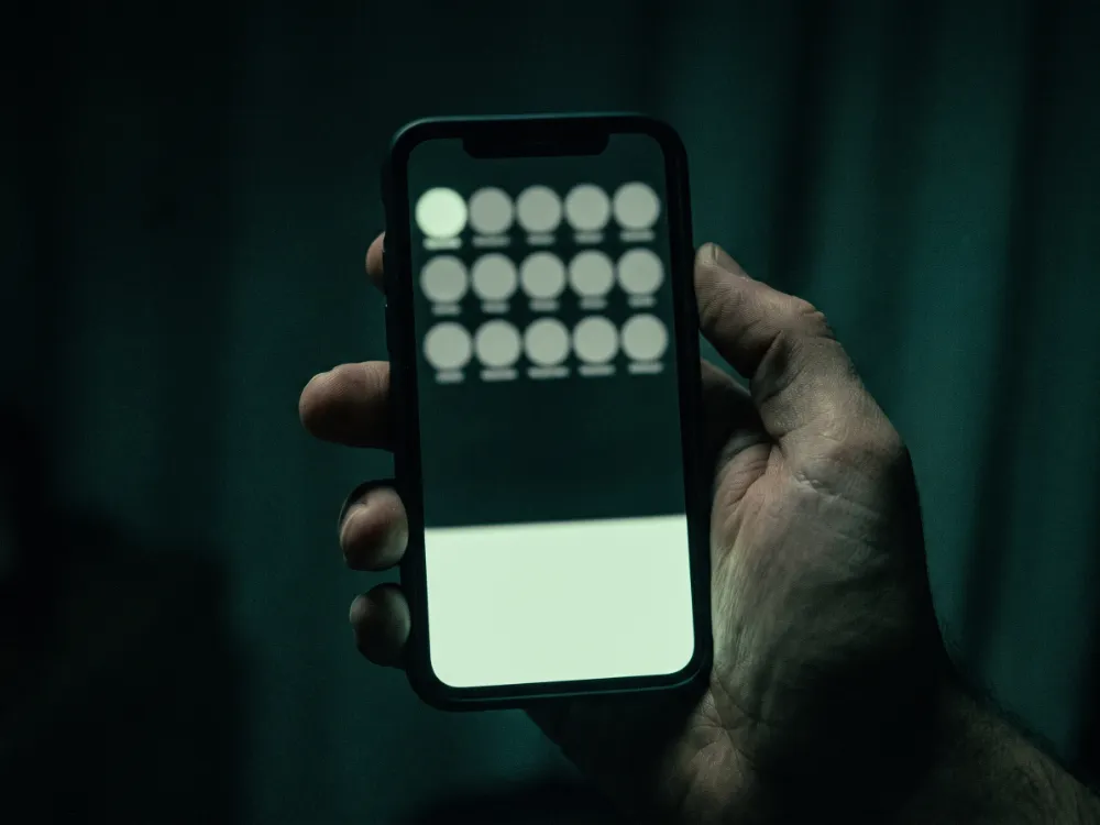 A hand holding a phone in the dark showing rows of speaker circles in a live audio room